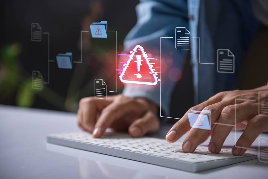 Hands typing on a keyboard with a red cybersecurity threat alert, surrounded by digital files and documents.
