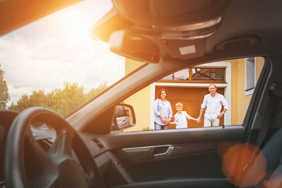 Home and Auto Insurance (Bundled) - From Inside the Car View of a Young Family Going to Their Car Standing in the Yard