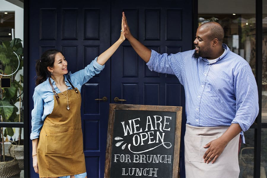 Business Insurance in New Hampshire - Cheerful Business Owners Standing with Open Sign Blackboard