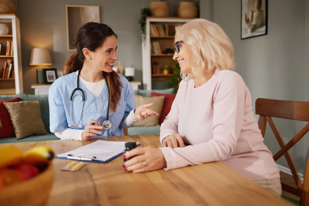 A nurse sitting at a table with a senior woman in her home.